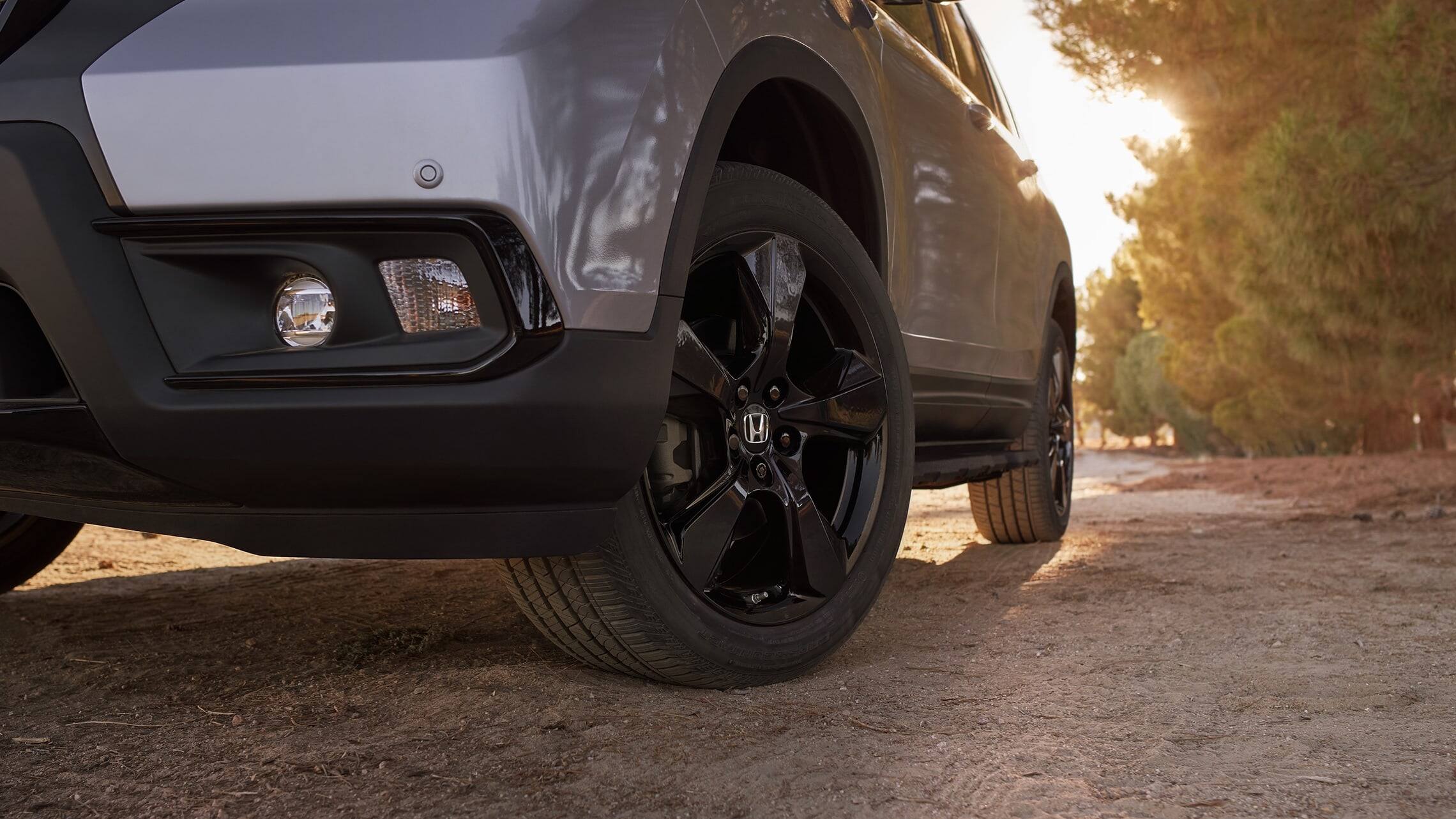 20-inch black alloy wheels on the 2019 Honda Passport Elite, in Lunar Silver Metallic with Honda Genuine Accessories, driving on a rugged road.
